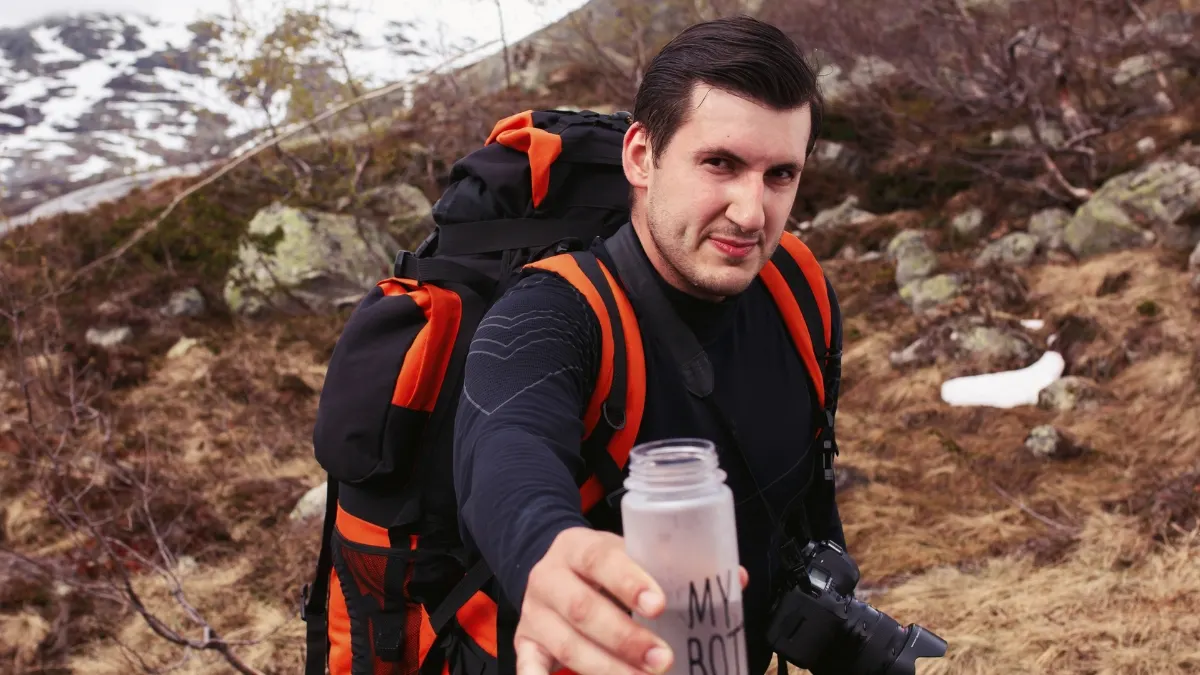 Hiker with backpack and water bottle in mountain terrain