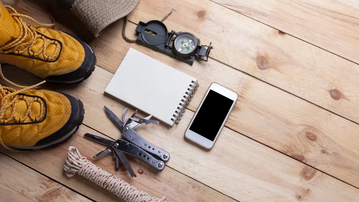 Survival gadgets flatlay — boots, compass, multi-tool, notebook